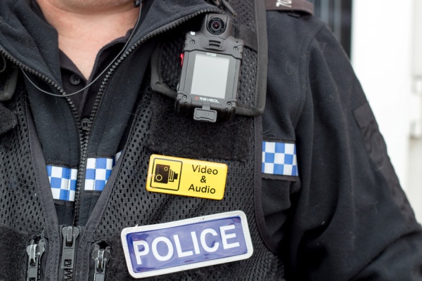 Close-up of police uniform jacket with body camera and yellow patch with camera icon and text stating Video and Audio.